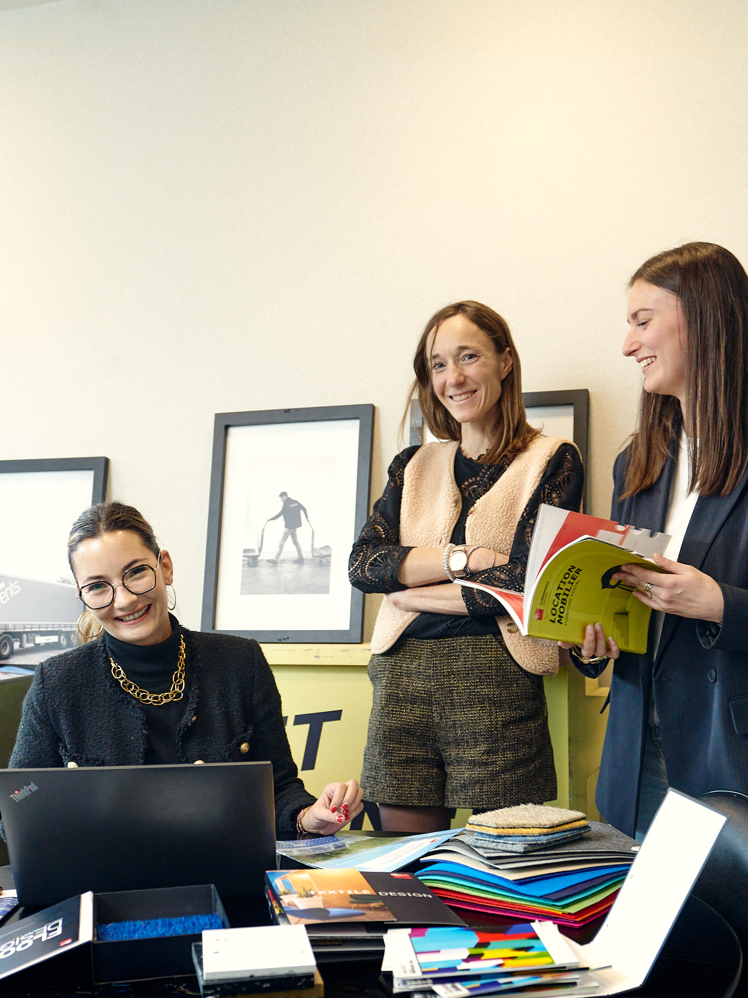 Trois collaboratrices réunies autour d’un espace de travail, échangeant sur des échantillons et documents, dans une ambiance professionnelle et conviviale.