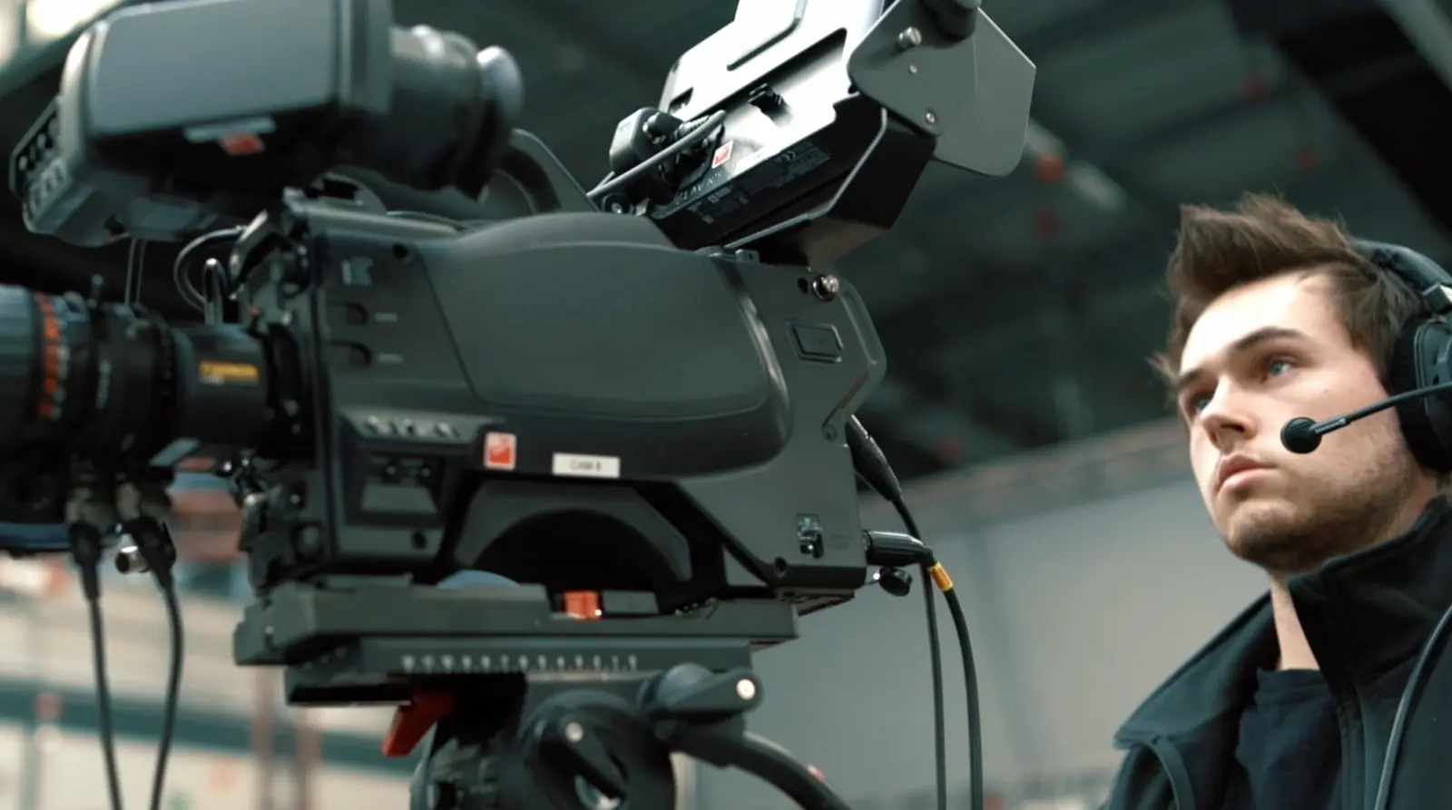 Technicien audiovisuel portant un casque micro opérant une caméra professionnelle sur trépied, concentré sur la captation d’un événement.