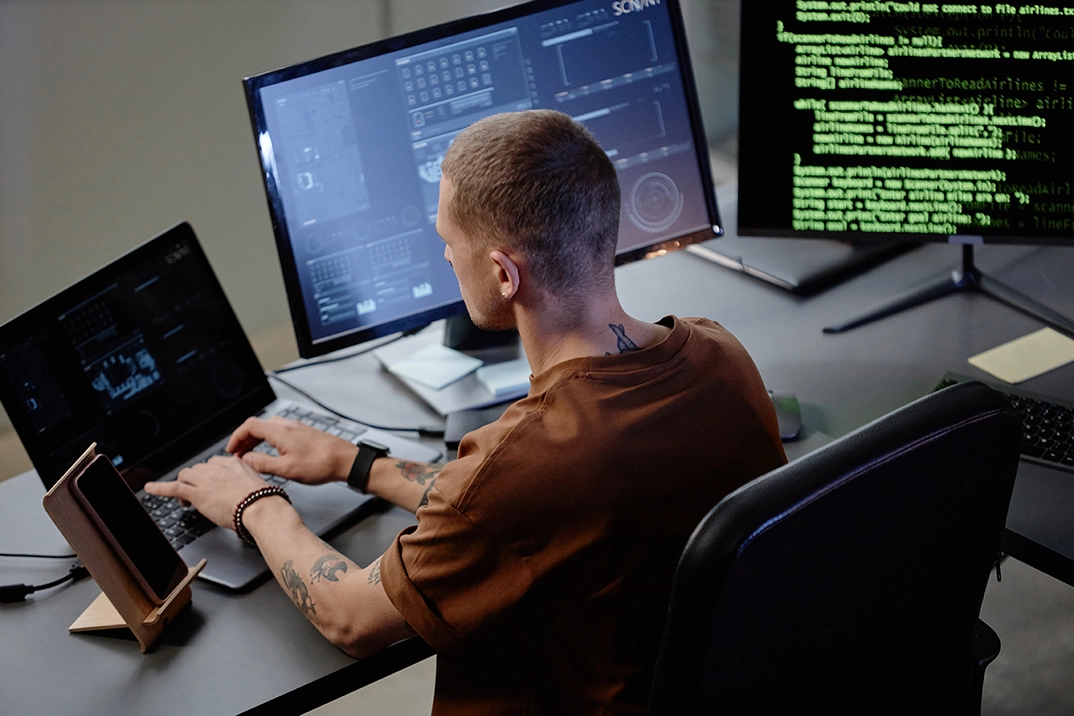 Un développeur travaille sur plusieurs écrans affichant du code et des interfaces, concentré sur son ordinateur dans un environnement de bureau.