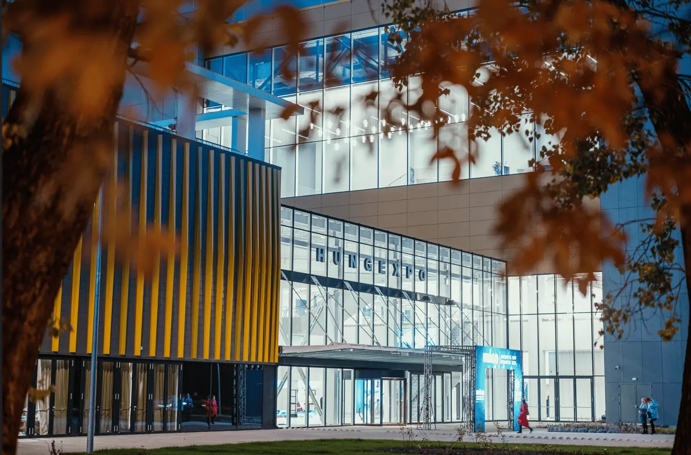 Un bâtiment d’exposition moderne, aux façades vitrées et lignes contemporaines, accueille des visiteurs dans un environnement dynamique, suggérant un lieu dédié aux événements, salons ou rencontres professionnelles.