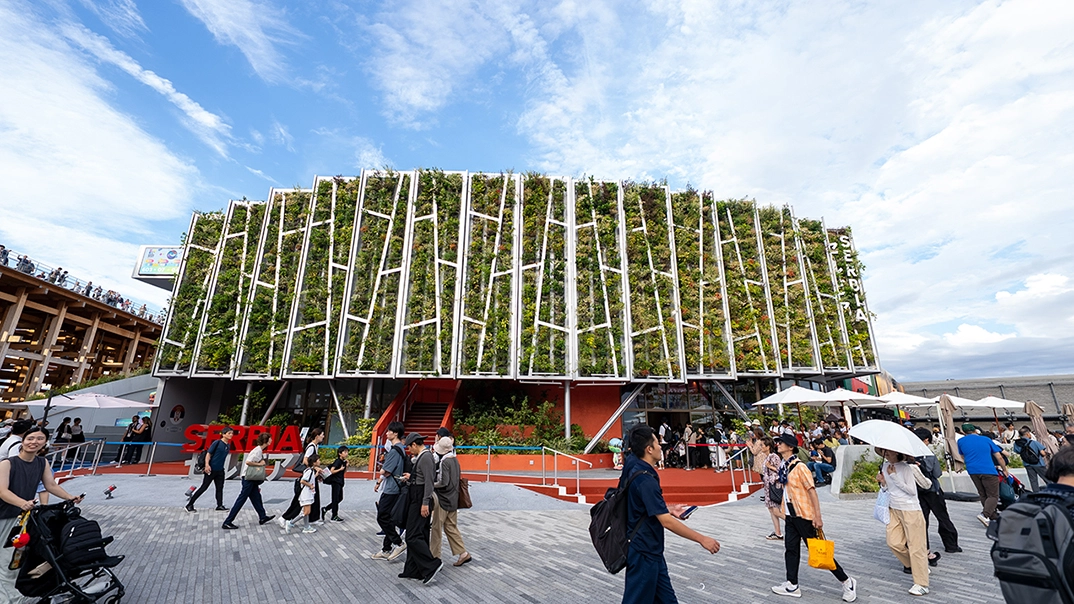 Un pavillon moderne recouvert de végétation accueille de nombreux visiteurs, dans un espace animé en plein air.
