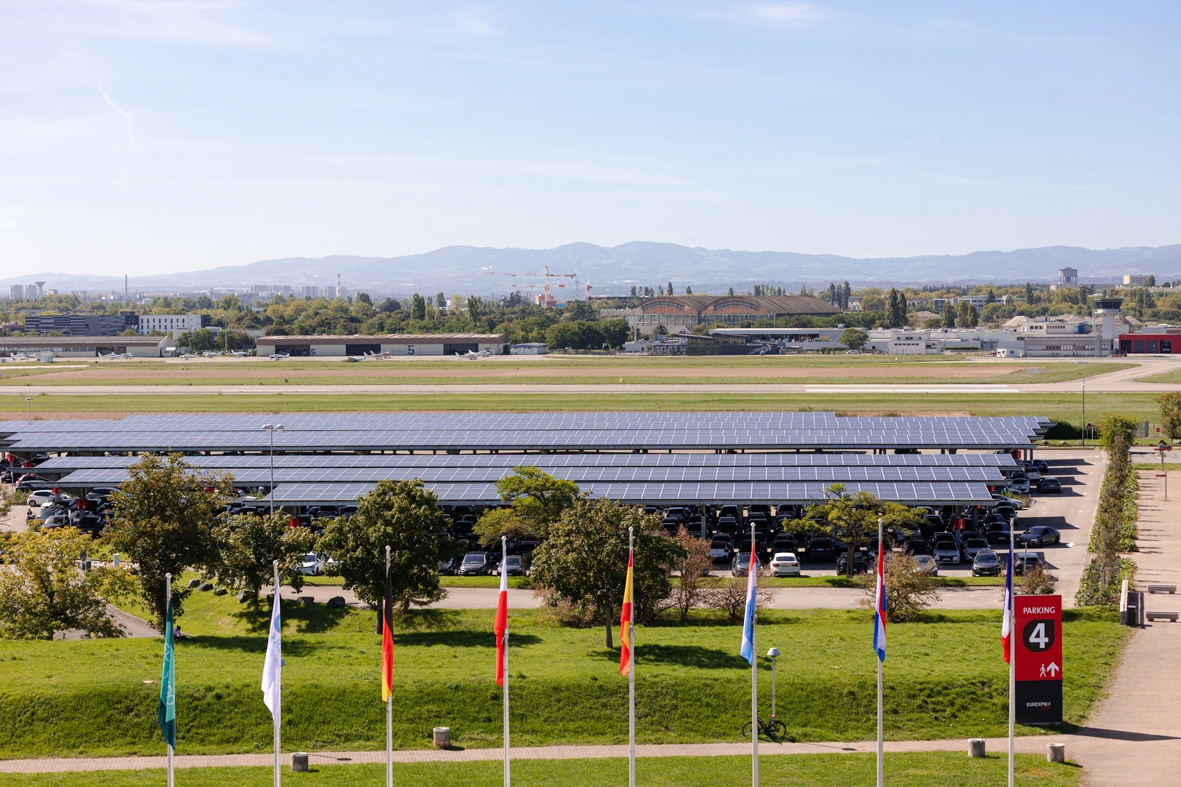 Vue extérieure d’un bâtiment moderne, partiellement entouré d’arbres, avec des panneaux solaires au premier plan, illustrant un site équipé d’installations d’énergie renouvelable. Sébastien Clavel