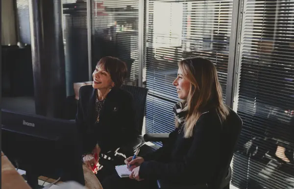 Deux femmes sont assises côte à côte dans un bureau, regardant un écran et prenant des notes dans une ambiance de travail collaborative. Alexandre Bagdassarian