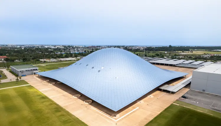 Un bâtiment emblématique à l’architecture audacieuse et fluide se déploie dans un vaste environnement ouvert, illustrant un lieu dédié aux grands événements, à l’innovation et à l’accueil de publics d’envergure.