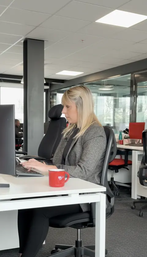 Une collaboratrice travaille à son poste dans un bureau moderne, concentrée sur son ordinateur. Sur le bureau, une tasse rouge siglée GL events apporte une touche de marque, tandis que l’environnement vitré et lumineux reflète un cadre professionnel contemporain et organisé. GL events