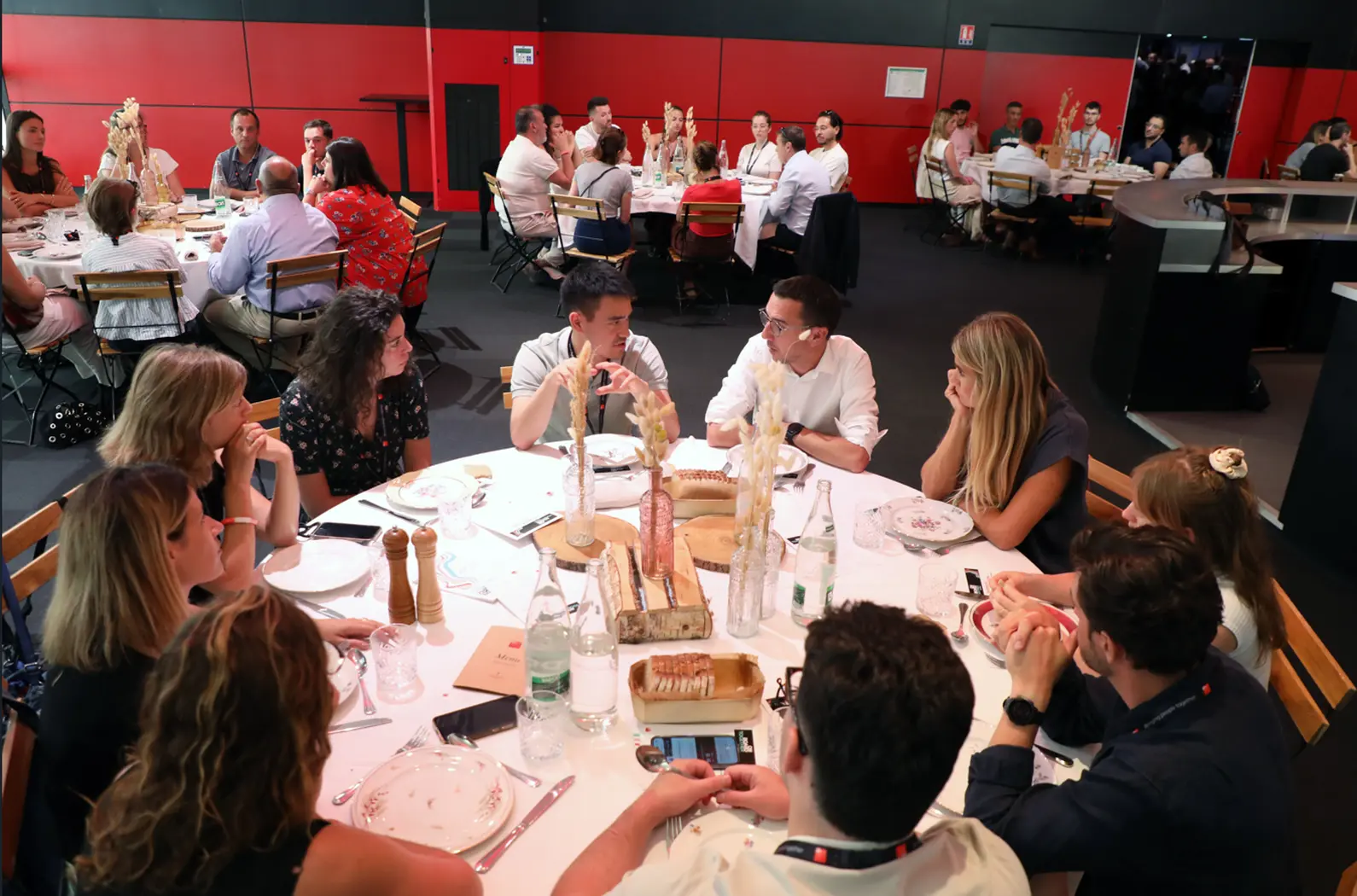 Des collaborateurs sont réunis autour de plusieurs tables rondes lors d’un repas dans une salle de réception, échangeant dans une ambiance conviviale propice aux discussions et au partage. Barbara Tournaire